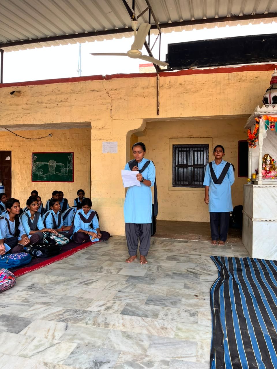 विद्यालय की एक छात्रा माइक पर कारगिल विजय दिवस पर अपना आलेख प्रस्तुत करते हुए, सामने बैठी छात्राएँ ध्यानपूर्वक सुनती हुईं